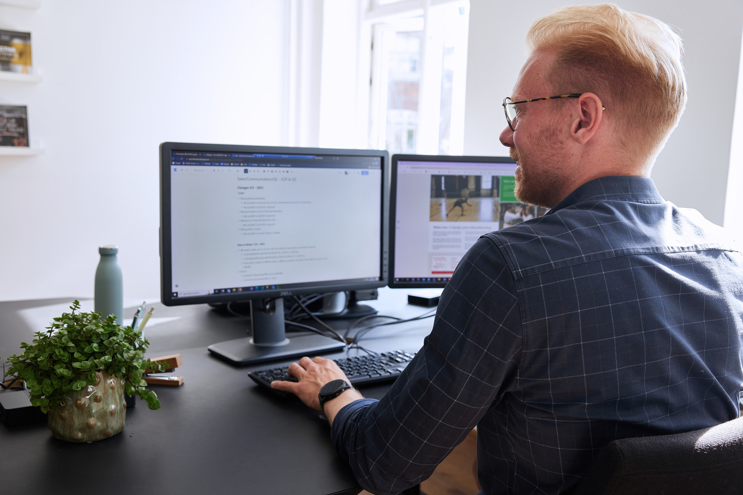 A smiling man is sitting at a desk and working at his computer.